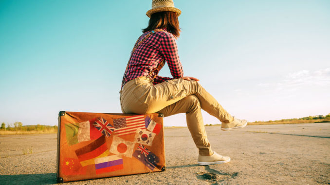 Traveler sits on suitcase with stamps flags