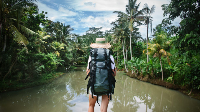 Woman,Traveler,With,Backpack,And,Hat,Standing,Near,Tropical,River